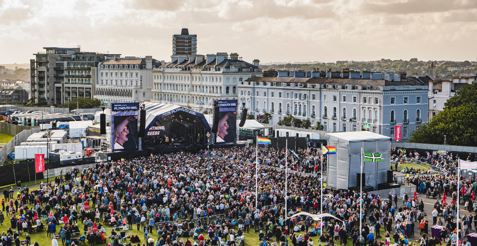 A music stage on Plymouth Hoe with buildings in the background and crowd looking on